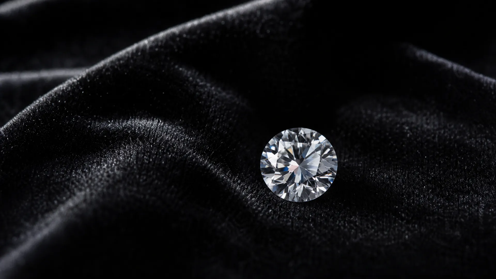A round brilliant diamond rests on black velvet under dramatic jewellery studio light.